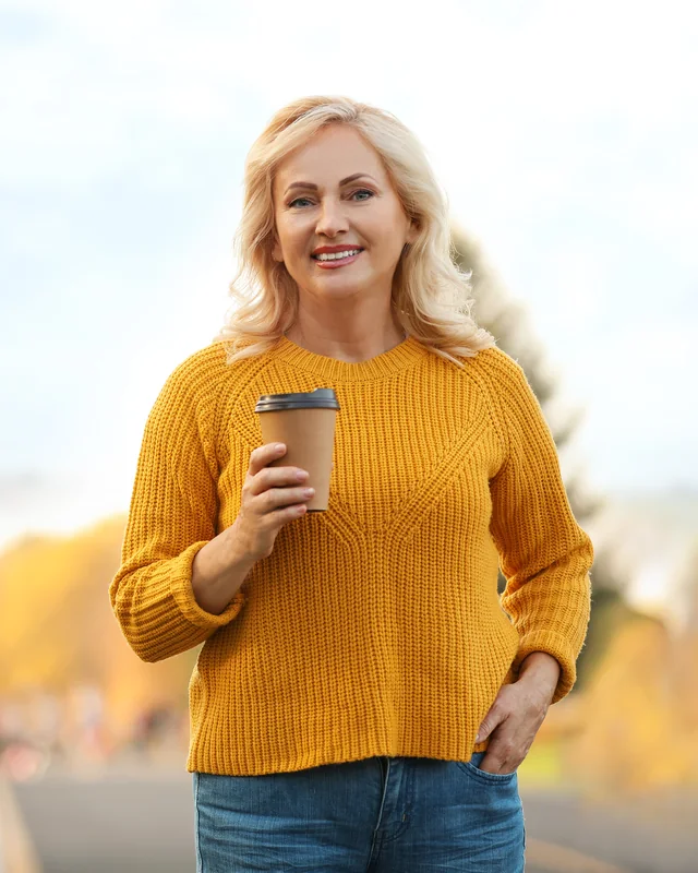 Mulher sorrindo ao ar livre em um dia de sol, com um copo de café na mão